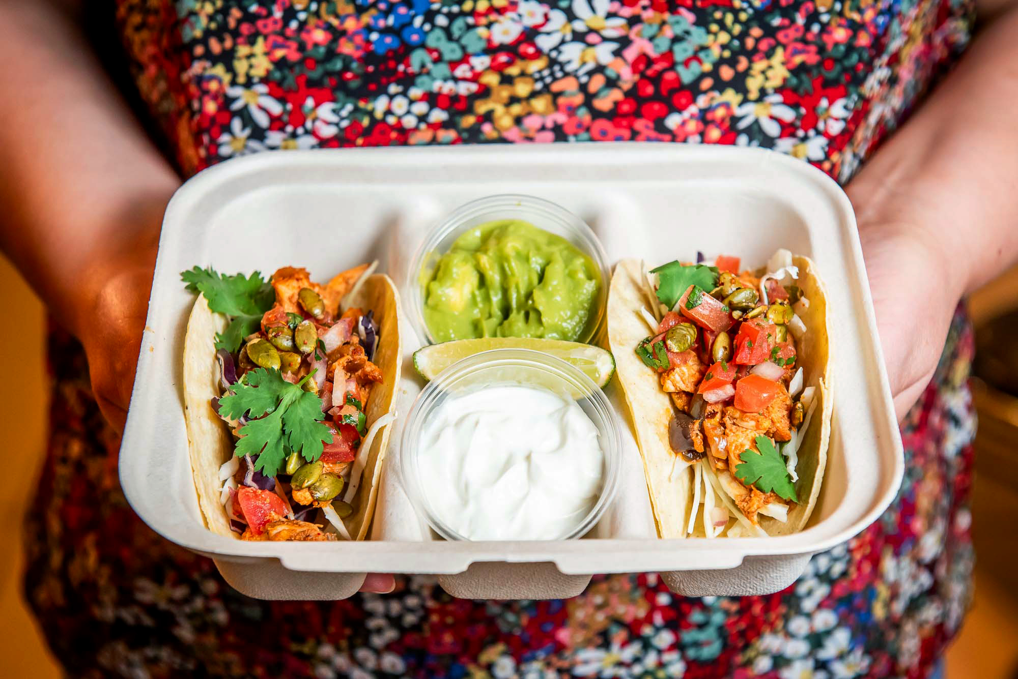 two hands hold box of tacos with gauc and sour cream
