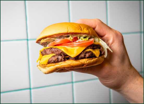 hands holding burger in front of white tile